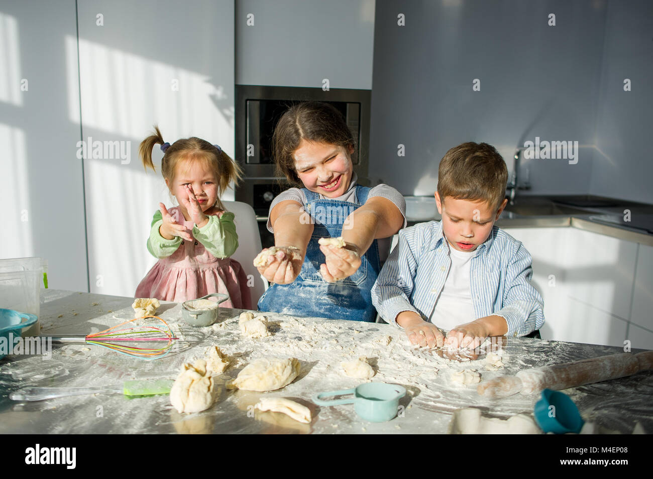 Tre bambini preparare qualcosa dall'impasto. Due sorelle e un fratello sono seduti al tavolo della cucina. Ci sono vari utensili di cucina sul Foto Stock