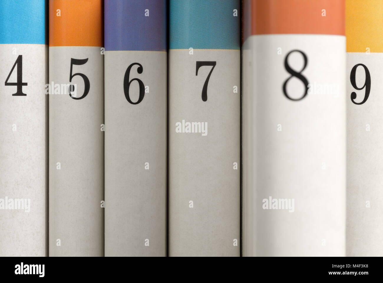 Sei colori di libri numerati con il numero di libro 8 parzialmente estratto dalla fila Foto Stock