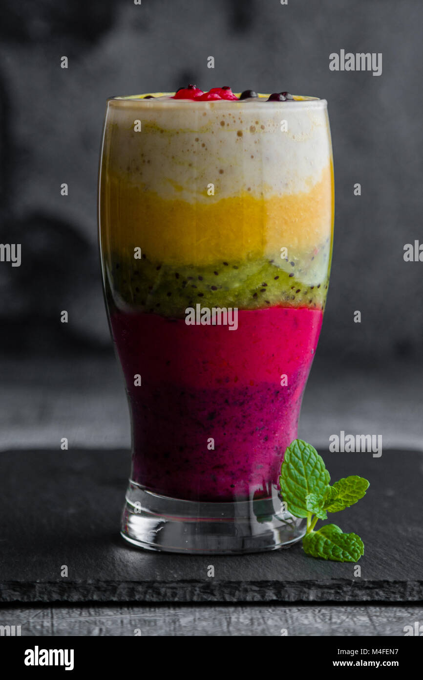 Frullato colorato fatto di frutti diversi stratificato in un bicchiere Foto Stock