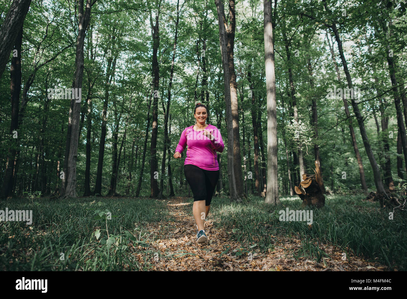 Vista frontale di un felice femminile cercando di mantenersi in forma e in esecuzione attraverso i boschi. Foto Stock