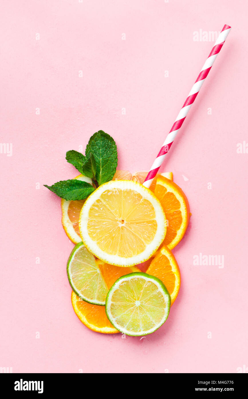 Bicchiere di succo di frutta fatta di fette di agrumi con foglie di menta e una paglia sulla luce sfondo rosa. Succo di agrumi concept Foto Stock