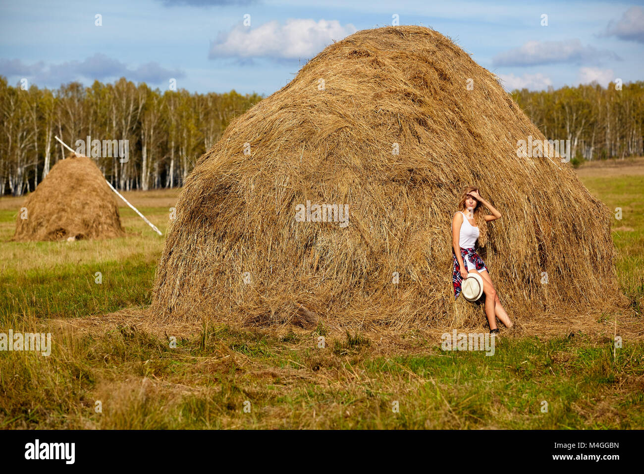 Giovane biondo country girl in hat vicino haystacks Foto Stock