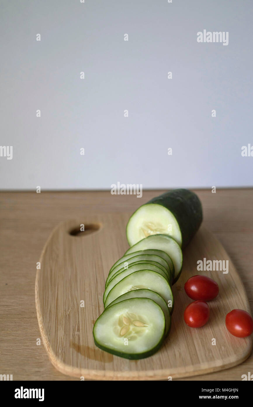 Cetriolo affettato e un paio di pomodori Uva su un tagliere Foto Stock
