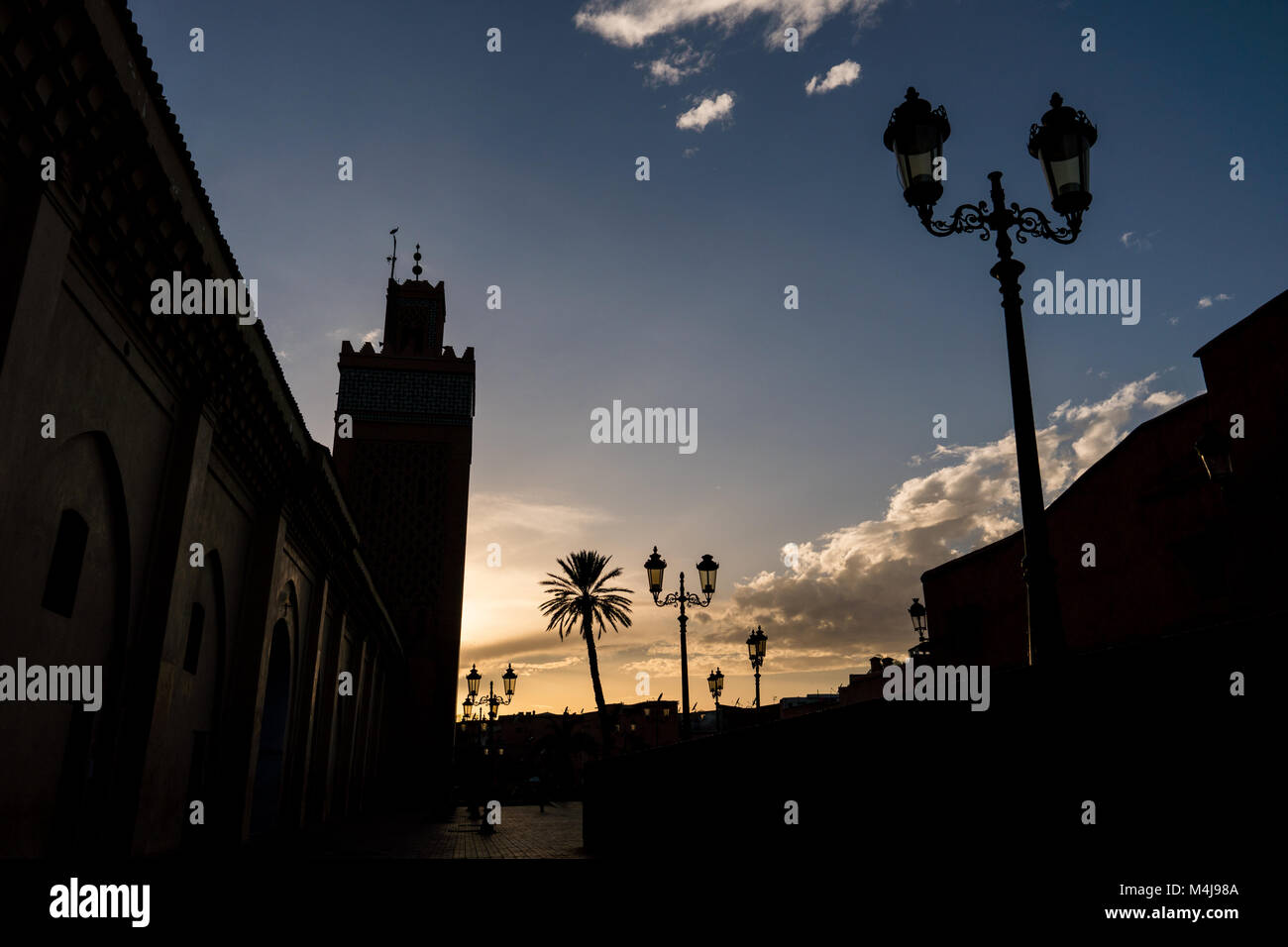 Silhouette di palme e candelabri street lights durante il tramonto a Marrakech, Marocco Foto Stock