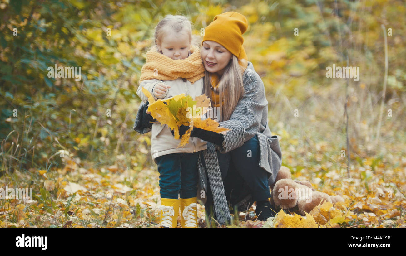La bionda bambina con la sua mamma passeggiate nel parco di autunno - sono divertenti e raccogliere foglie, close up Foto Stock
