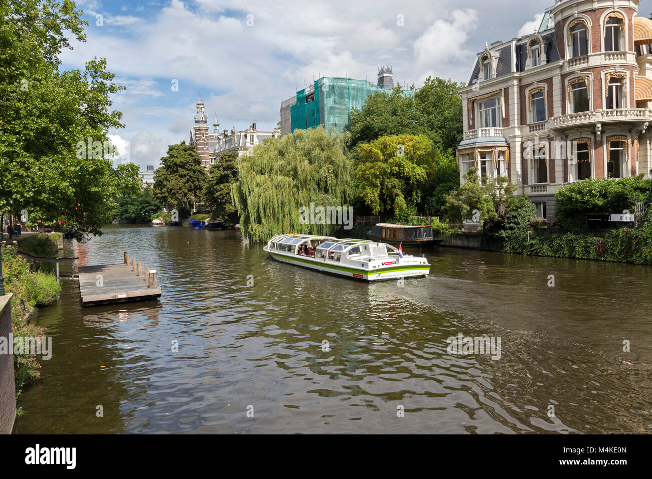 Vista di un viale alberato canal con, hop on hop off tour barca piena di turisti. Questo spot è situato di fronte al famoso Rijksmuseum. Foto Stock