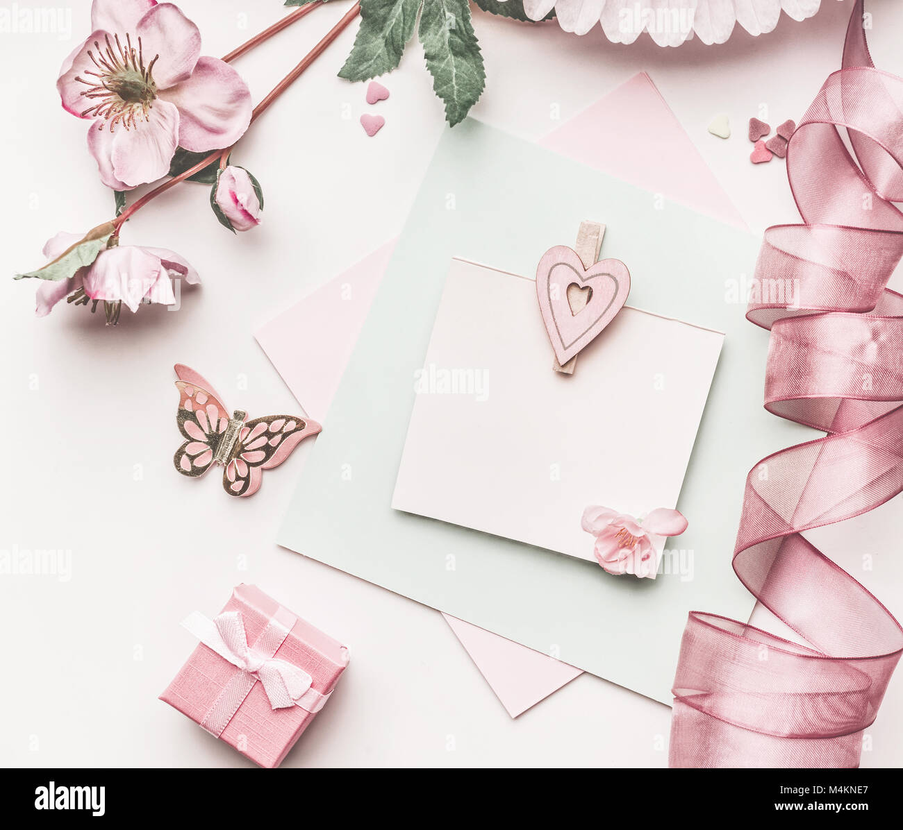 Bella rosa pastello formato con decorazioni di fiori,nastro, cuori e carta mock up bianco su sfondo scrivania, vista dall'alto, piatto laici. Invito a nozze, Foto Stock