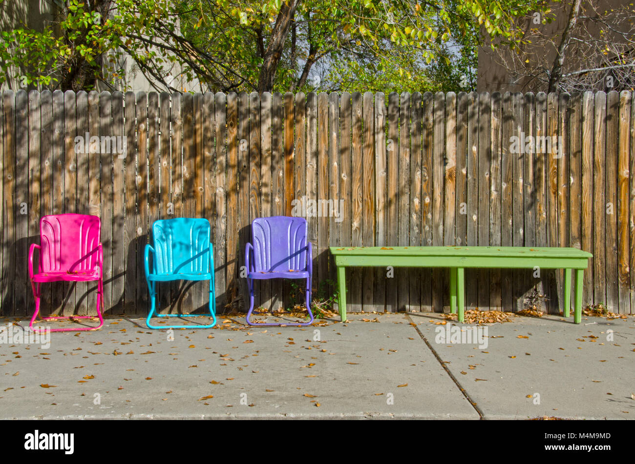 Tre colorate sedie di prato sit vuoto contro una staccionata in legno, con le foglie di autunno sparsi tra loro. Foto Stock