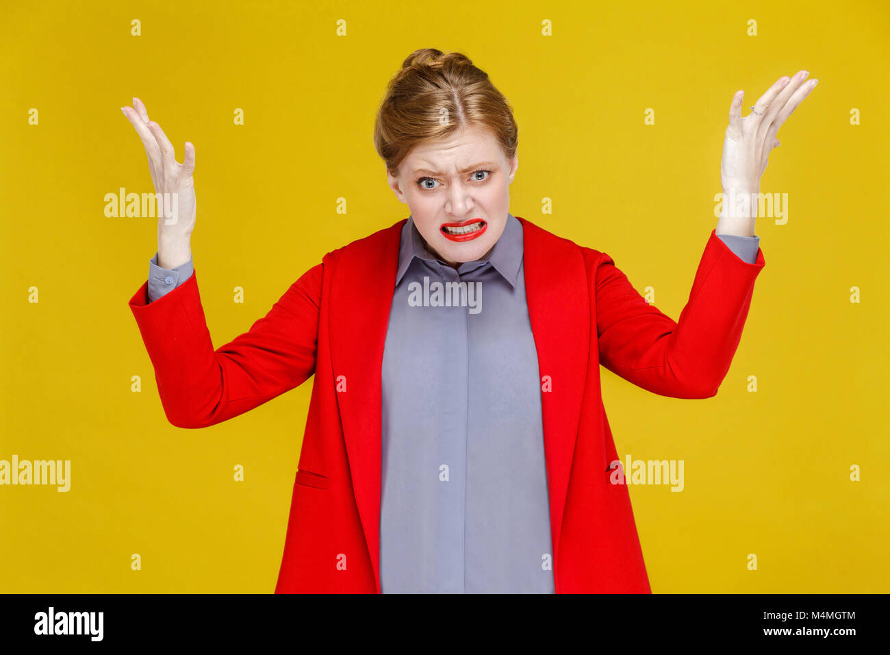 Arrabbiato redhead Woman in Red Suit ruggito. Studio shot, isolato su sfondo giallo Foto Stock