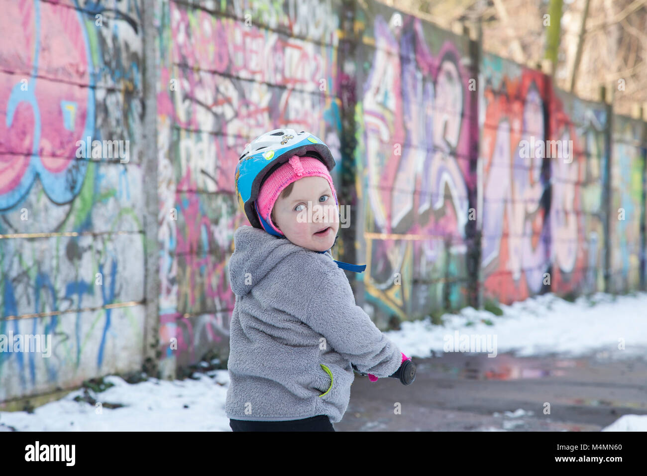 Felice bambina divertirsi nella natura accanto al muro di graffiti e imparare a cavalcare la sua prima moto Foto Stock