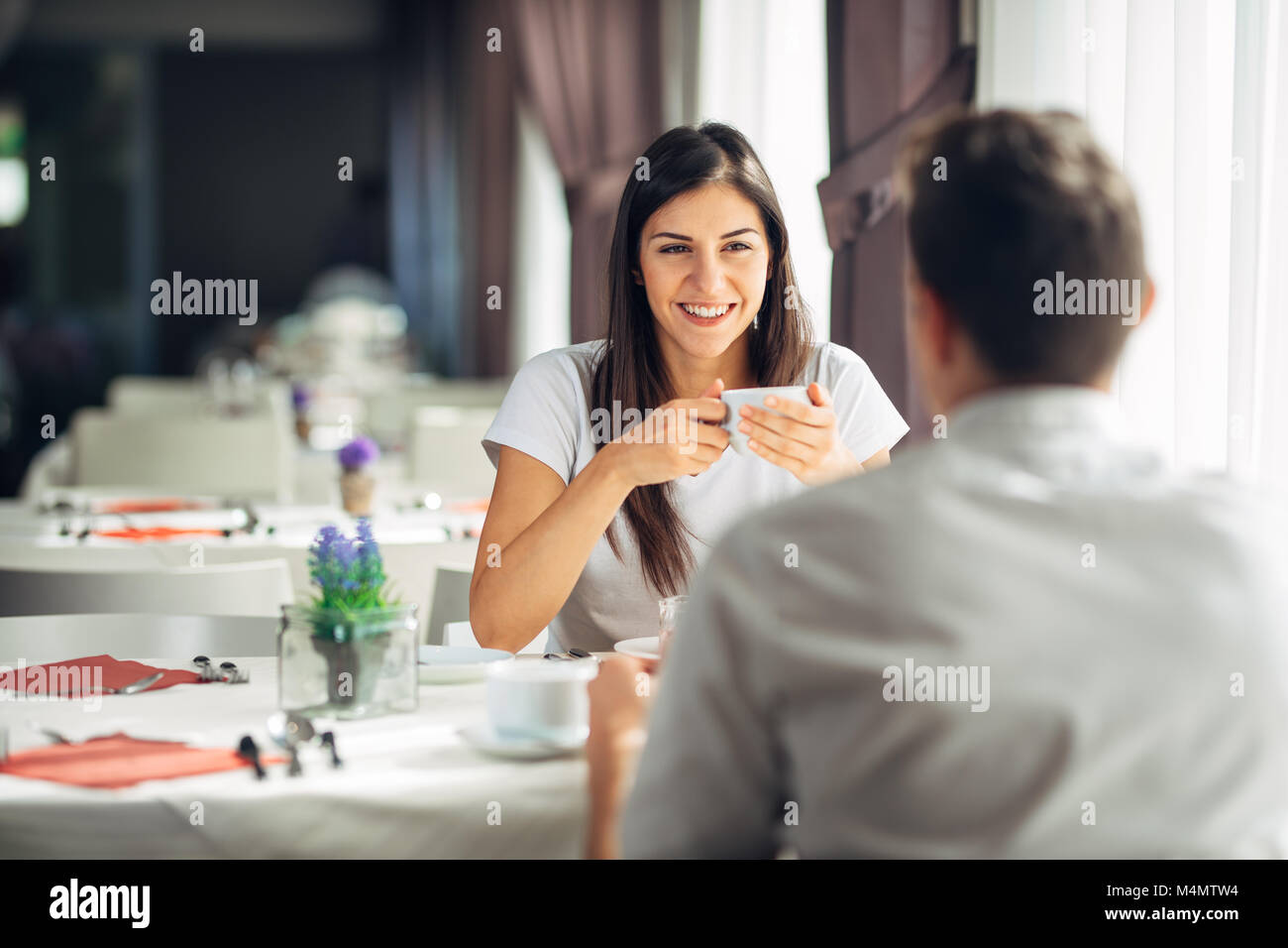 Donna sorridente su una data in un ristorante,avente una conversazione con un pasto in hotel.Allegro cliente femmina di bere il caffè con un partner.em positivo Foto Stock