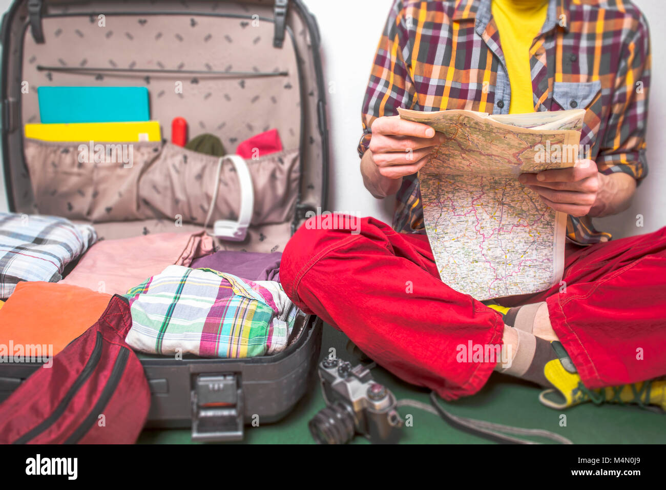 Un uomo è la pianificazione di un viaggio, un viaggio turistico, guardando una mappa, un aprire la valigia. Foto Stock