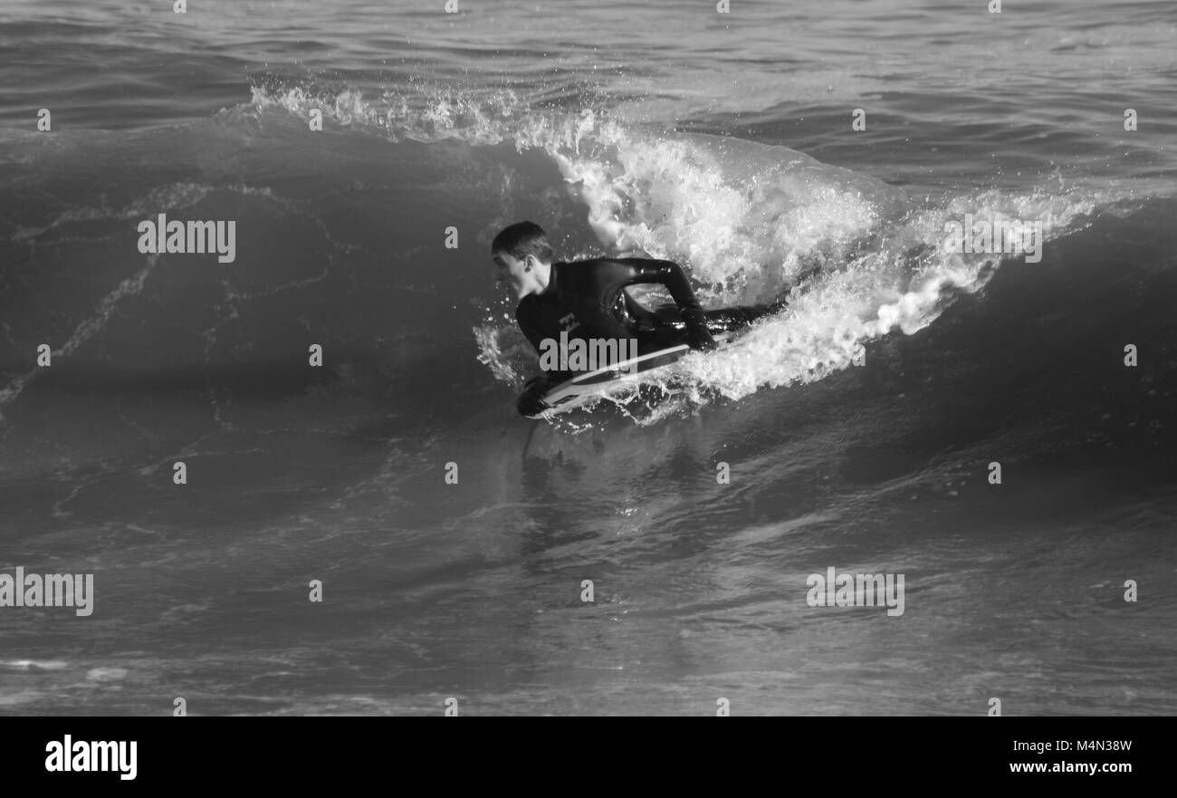 Drammatica foto in bianco e nero di un audace Bodyboarder maschio Surf freddi del Nord onde del mare presso la spiaggia di Aberdeen, Scozia, Regno Unito. Inverno 2018. Foto Stock