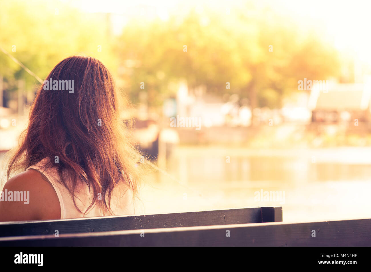 Giovane donna seduta su una panchina a guardare il dock della baia al tramonto, Rotterdam, Paesi Bassi Foto Stock