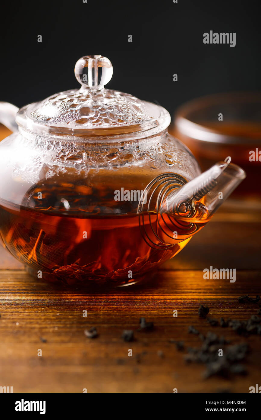 Vetro trasparente tè pentola con acqua calda tè nero su un tavolo di legno. Chiudere verticale up shot. Foto Stock
