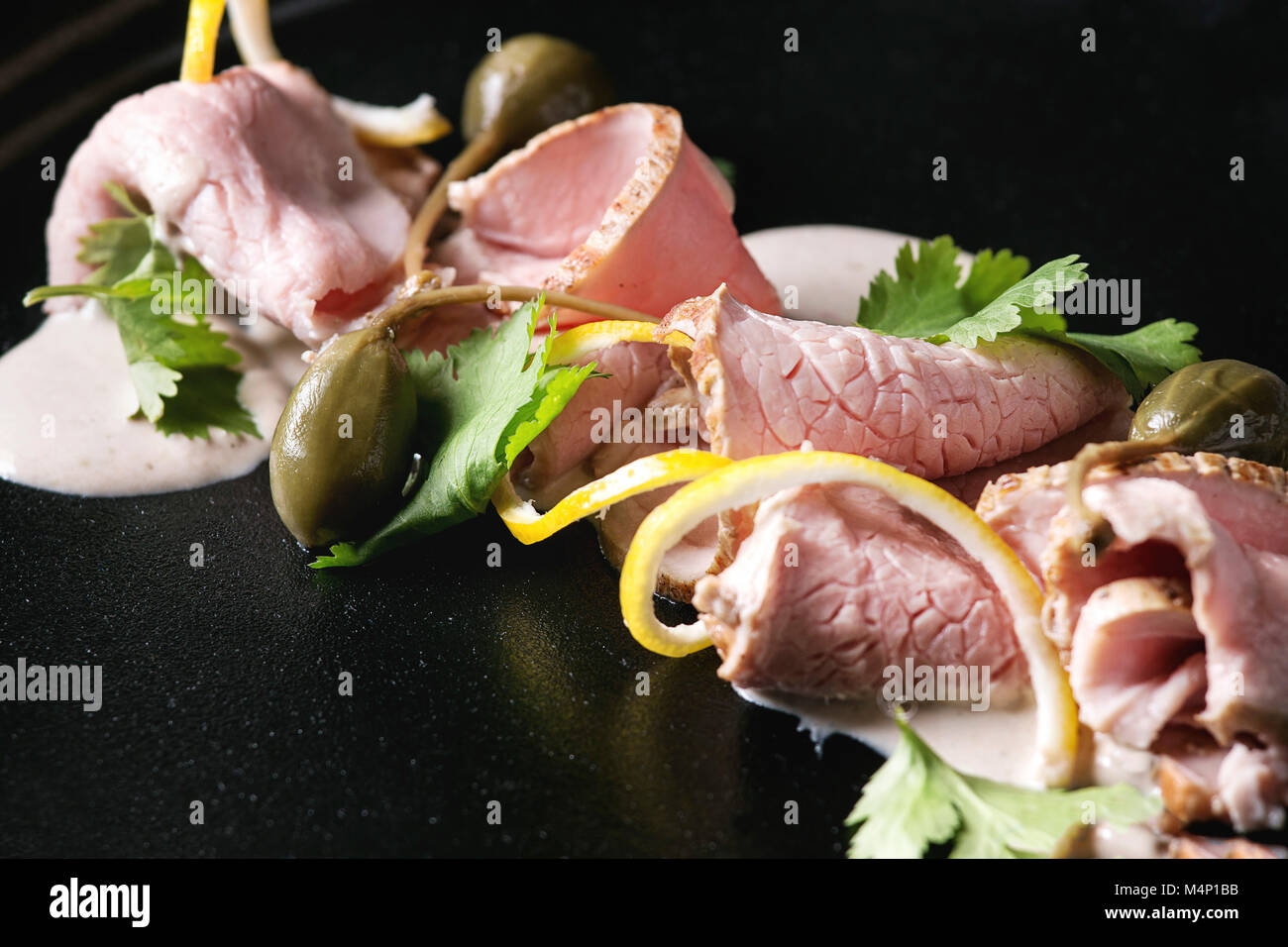 Vitello tonnato piatto italiano. Sottili fette di vitello con salsa di tonno, capperi e coriandolo servita su piastra nera. Close up Foto Stock