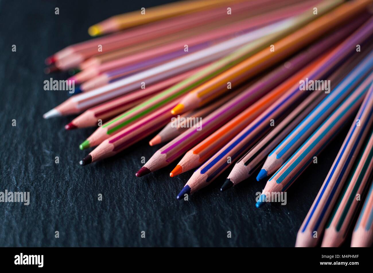 Un array di matite colorate disteso su un nero ardesia Foto Stock