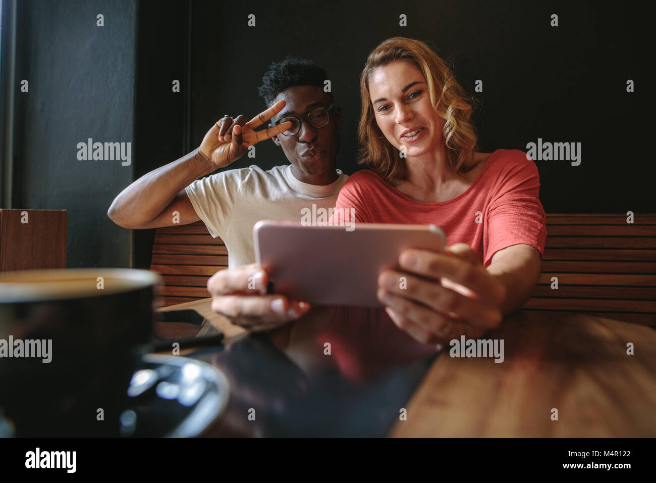 Sorridente giovane prendendo un selfie tramite telefono cellulare seduti ad un tavolo da caffè. L uomo e la donna la condivisione di momenti felici in un coffee shop. Foto Stock