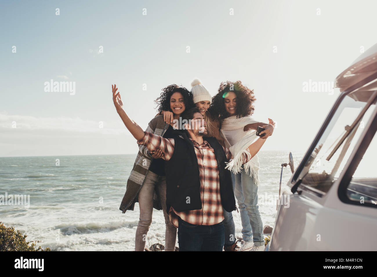 Amici in viaggio su strada tenendo selfie con il telefono cellulare. Un gruppo di uomini e donne che assumono ritratto di auto all'aperto. Foto Stock