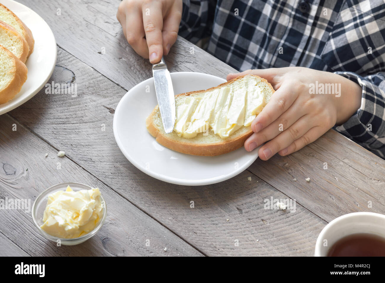 Mani maschio diffusione di burro sul pane tostato mentre la mattina a colazione. La prima colazione a casa con pane burro e tè. Foto Stock