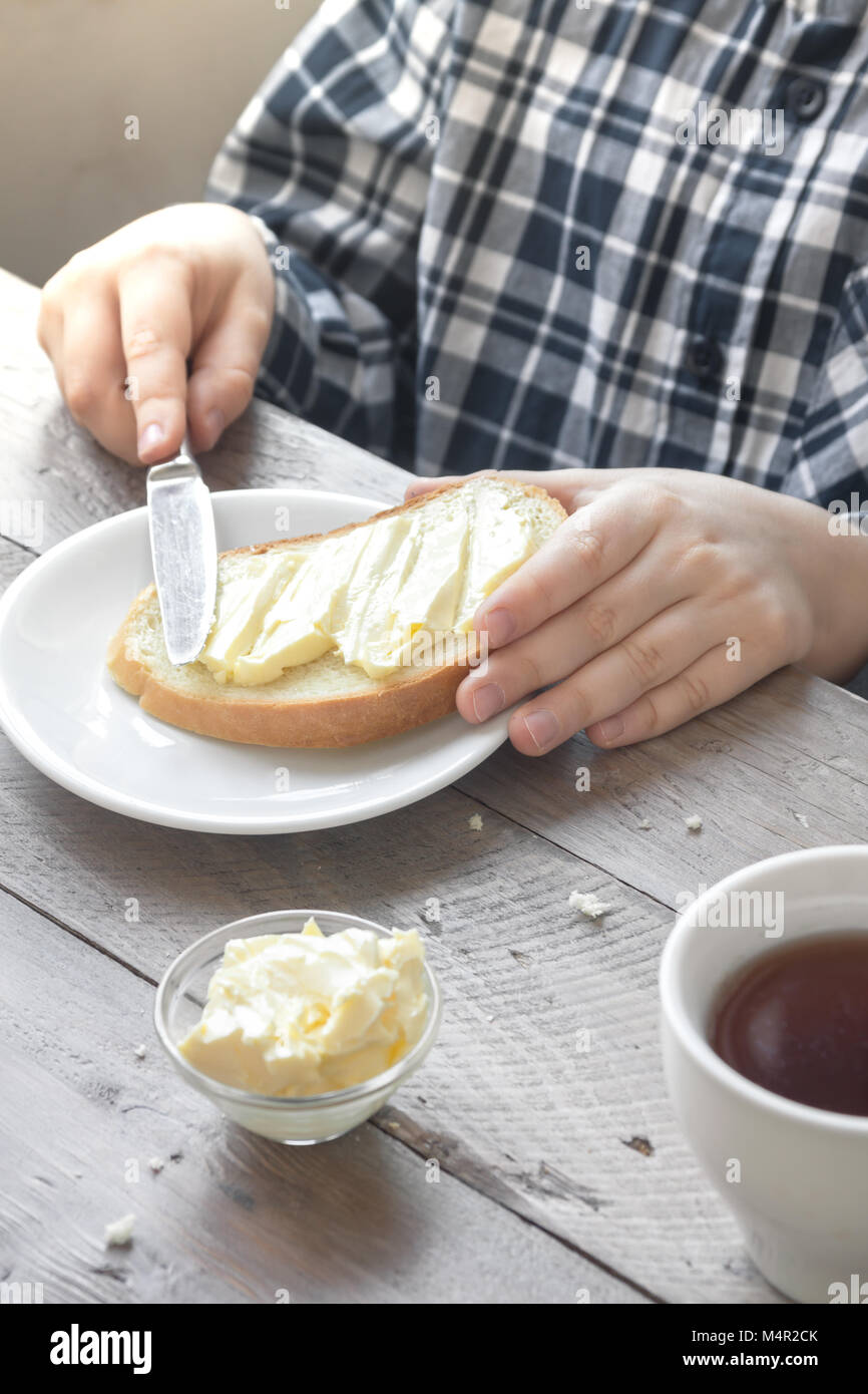 Mani maschio diffusione di burro sul pane tostato mentre la mattina a colazione. La prima colazione a casa con pane burro e tè. Foto Stock