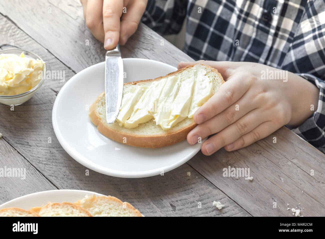 Mani maschio diffusione di burro sul pane tostato mentre la mattina a colazione. La prima colazione a casa con pane burro e tè. Foto Stock