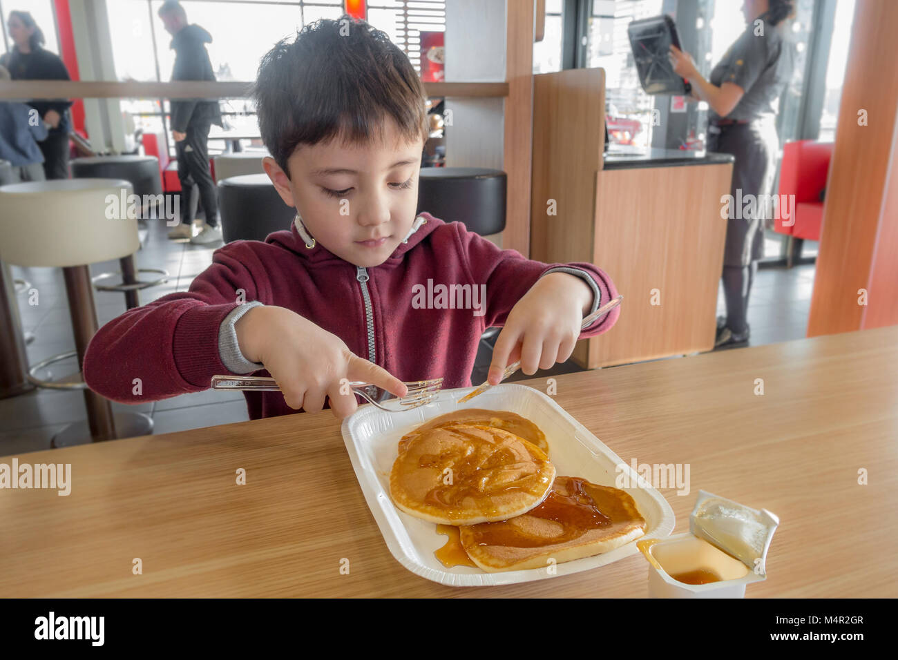 Come un regalo, un giovane bambino gode di pancake con sciroppo per fare colazione in un ristorante McDonalds. Foto Stock