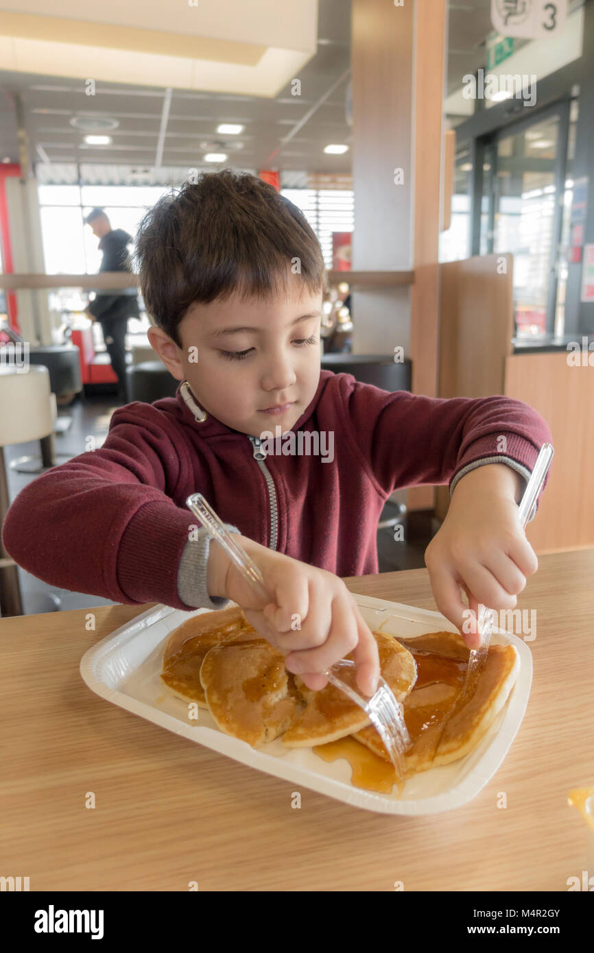 Come un regalo, un giovane bambino gode di pancake con sciroppo per fare colazione in un ristorante McDonalds. Foto Stock