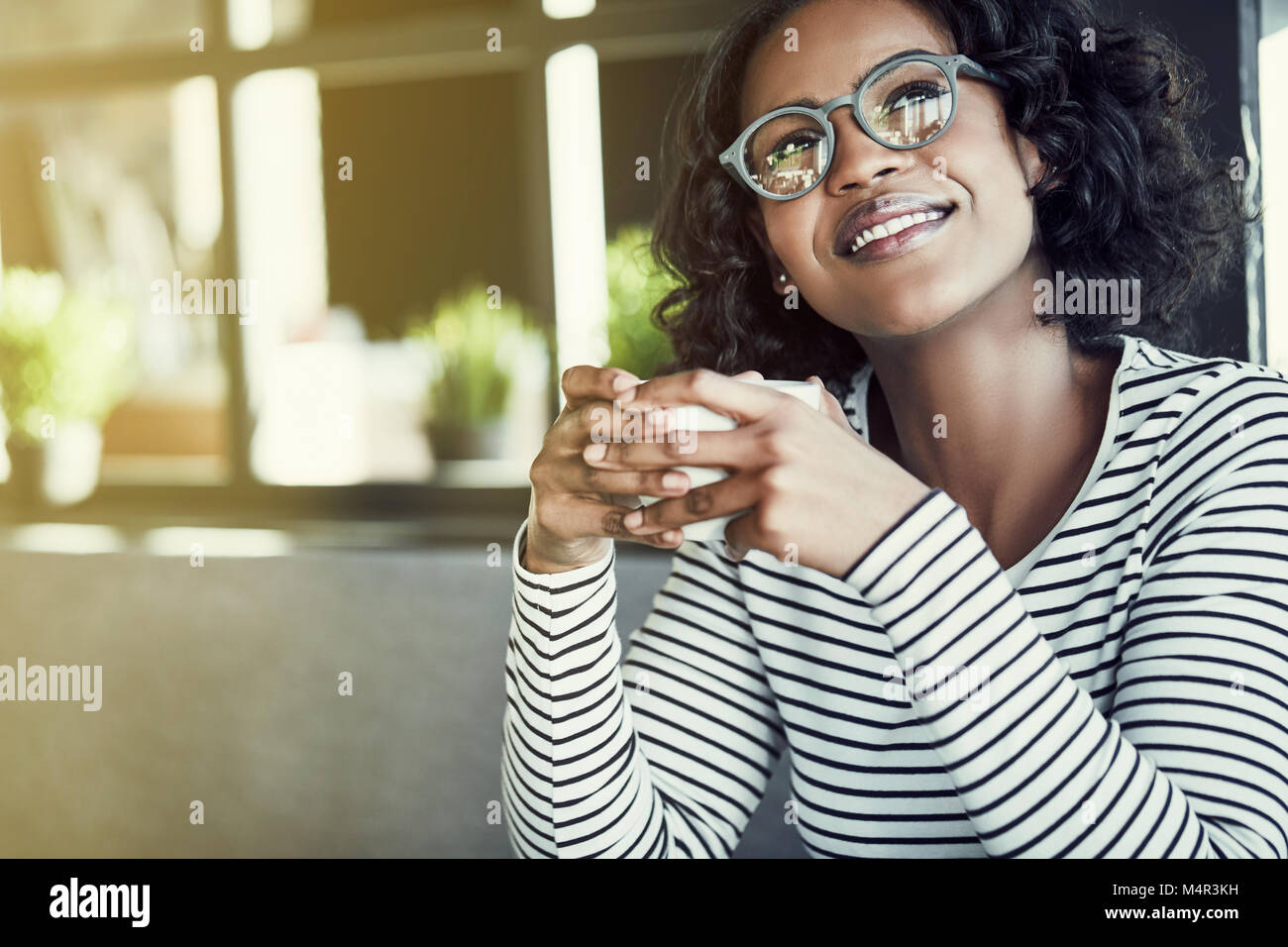 Sorridente giovane donna africana di bere un fresco bicchiere di caffè mentre è seduto da solo ad una tabella in un cafe Foto Stock