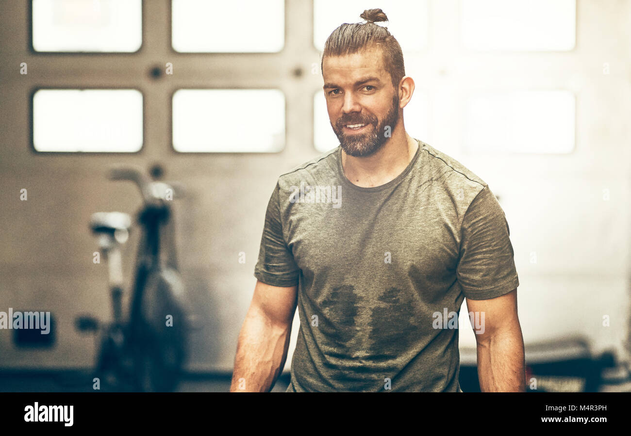 Montare il giovane uomo in sportswear sorridere mentre in piedi da solo in una palestra sudorazione dopo una sessione di allenamento Foto Stock