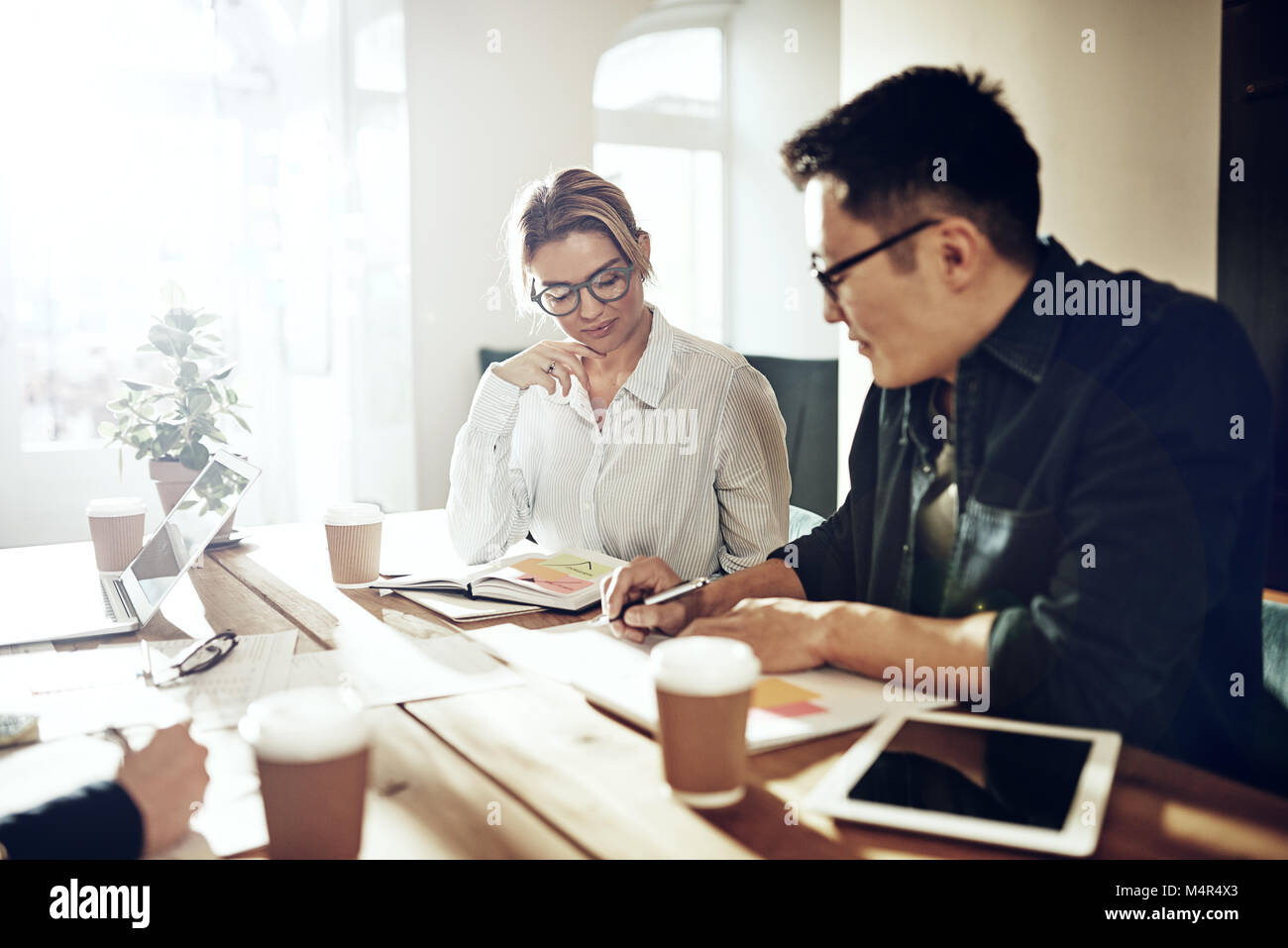 Due diversi colleghi concentrata sulla discussione di documenti cartacei insieme seduti a un tavolo in un ufficio moderno Foto Stock