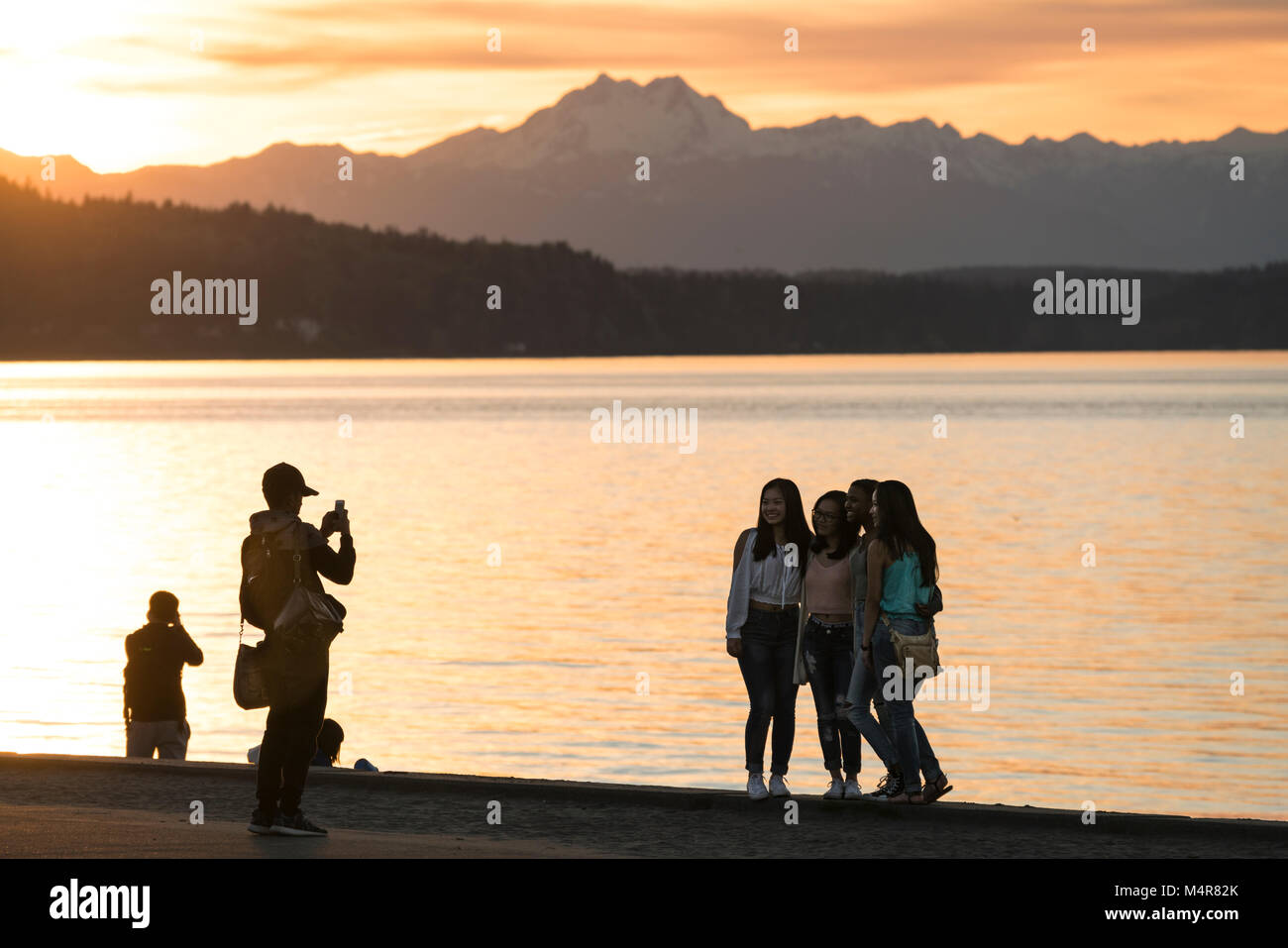 Un gruppo di giovani donne di ottenere le loro foto scattata sul Alki Beach con le Montagne Olimpiche dietro, Seattle, Washington, Stati Uniti d'America Foto Stock