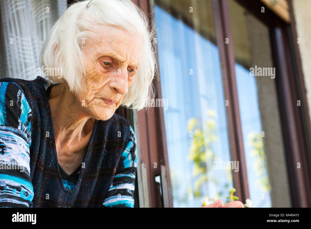 Senior donna guardando fuori della finestra di casa da solo Foto Stock