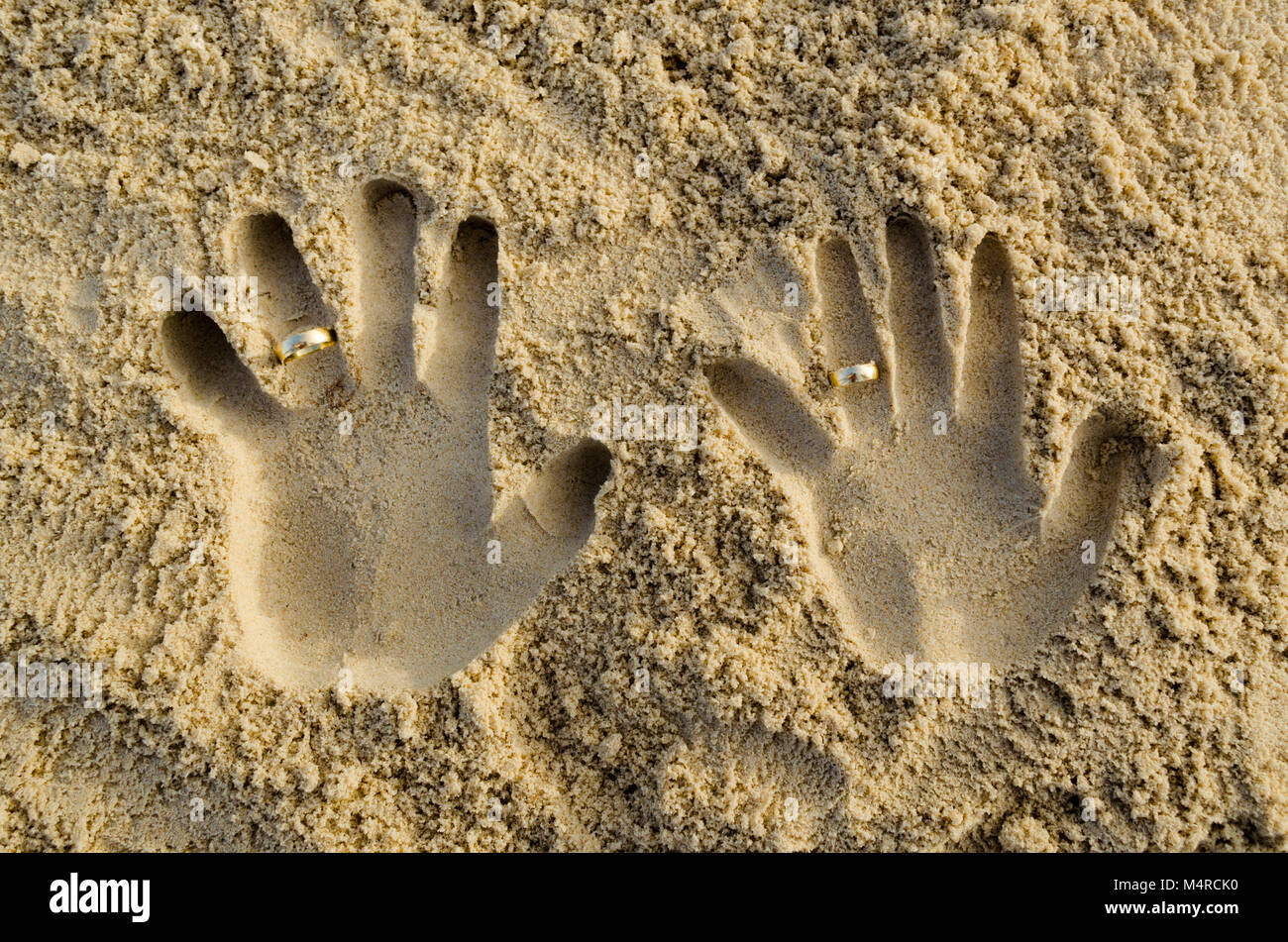 A due mani in forma di sabbia con gli anelli di nozze sulla corona dita. Sensazione di unione, giovane, passione e compagnia Foto Stock