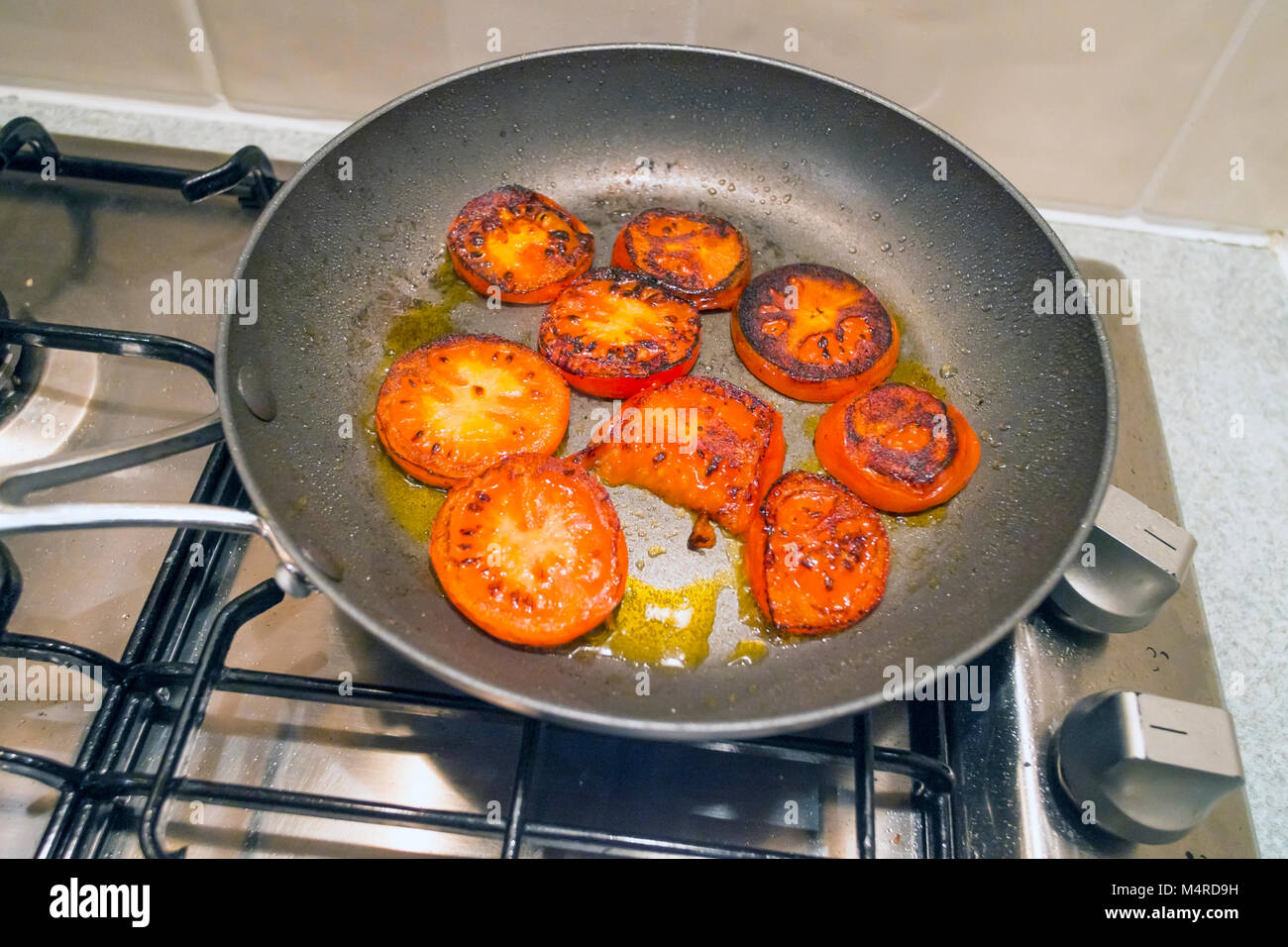 Pomodori a fette essendo fritto in olio di oliva in una piccola rivestita  in teflon antiaderente padella su un piano cottura a gas Foto stock - Alamy