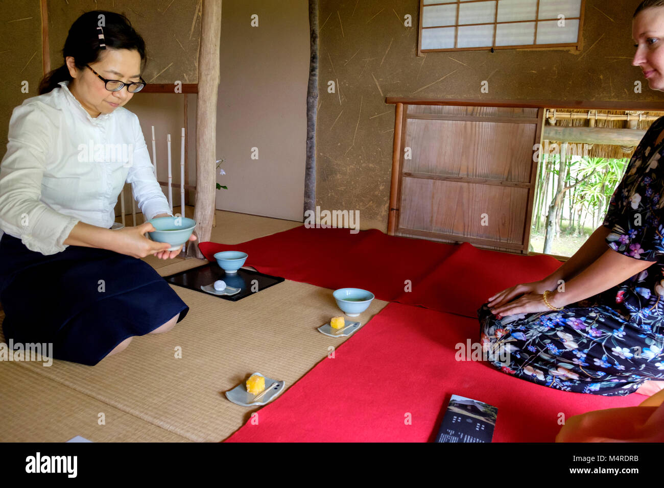 Chinshin cerimonia del tè con hostess holding tazza da tè, seduti su stuoie di bambù e valutazione guardando da un tappeto rosso. Dolci tradizionali sono già serviti. Foto Stock