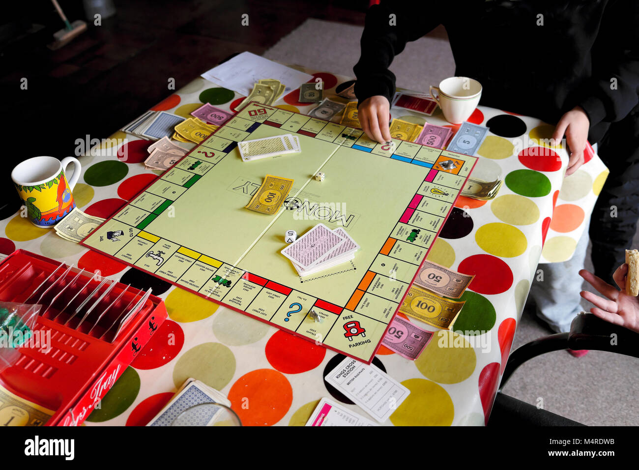 Scheda di monopolio gioco che viene giocato da bambini amici all'interno di una casa su un tavolo con la tovaglia colorato a metà termine in Carmarthenshire Wales UK Foto Stock