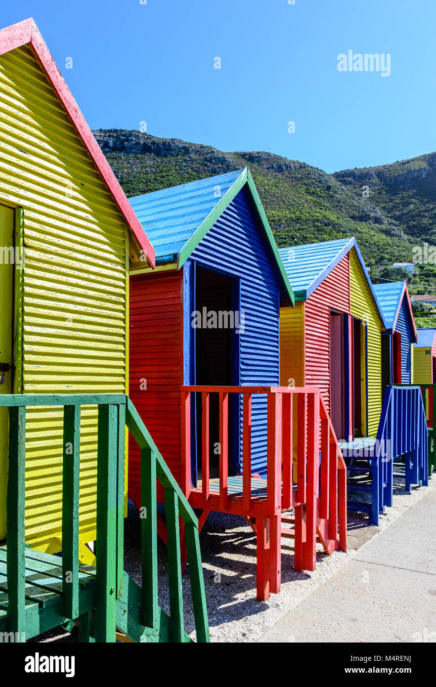 Famoso Vittoriano colorate scatole di balneazione presso San Giacomo Beach, Città del Capo, Sud Africa, presa su un soleggiato chiaro luminoso giorno sotto il cielo blu con le colline Foto Stock