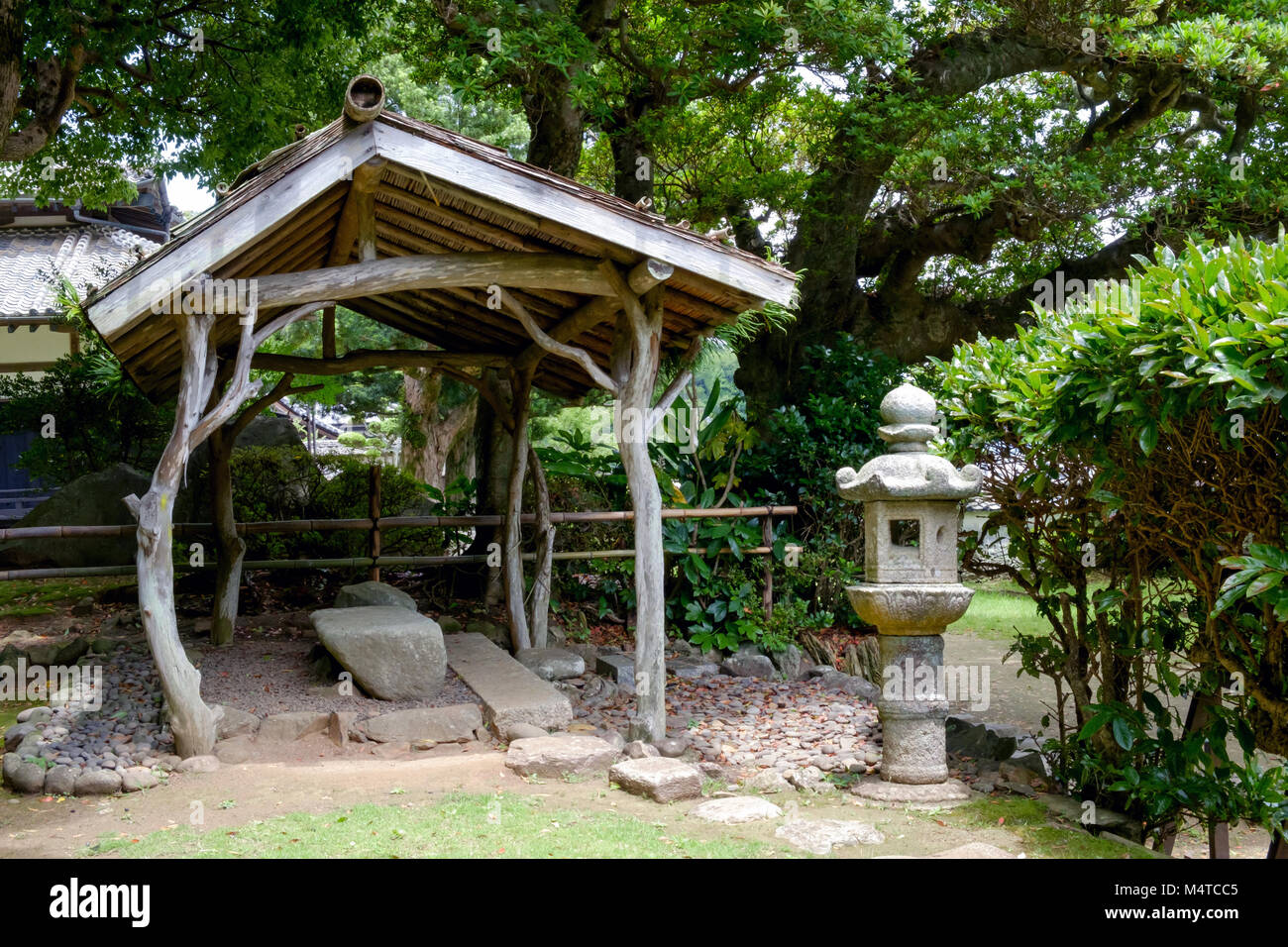 Giardino a Matsura Museo Storico, Hirado, di Nagasaki, Giappone. Struttura in stile rustico con tetto in centro, pietra memoriale sulla destra. Alberi, rocce e cespugli. Foto Stock