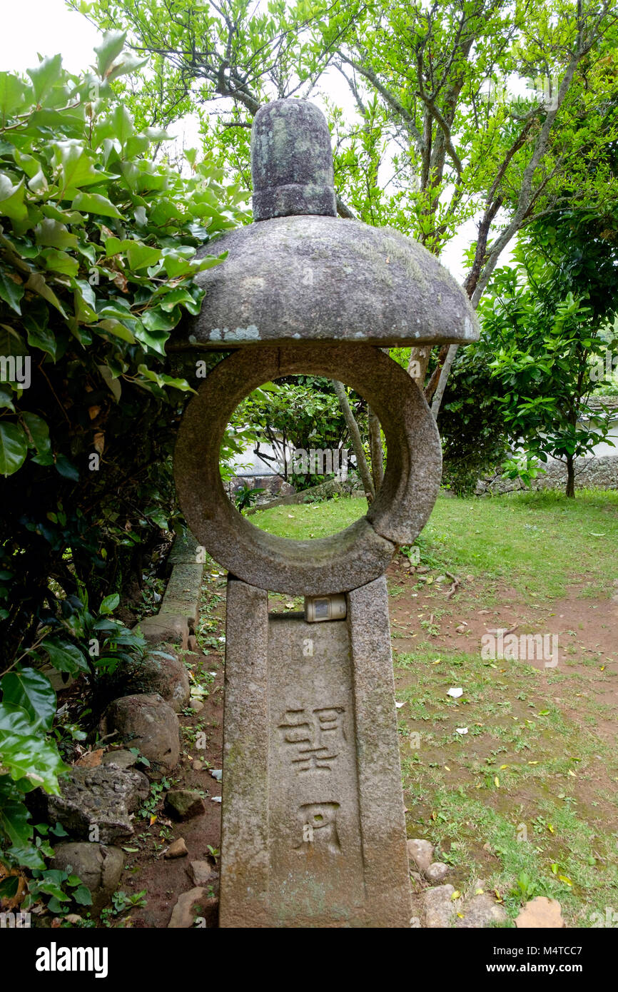 Giardino Zen, Matsura Museo Storico, Hirado, di Nagasaki, Giappone. Alberi ed erba. Close up della vecchia pietra circolare memorial giapponesi con parole incise. Foto Stock