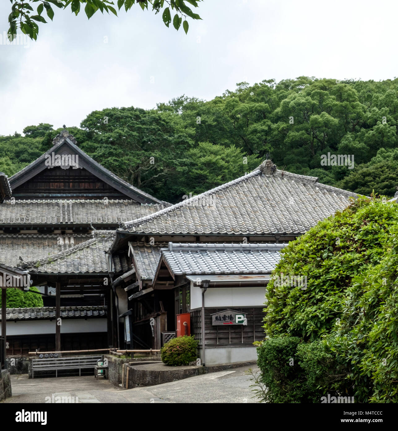 Tradizionali edifici giapponesi con alberi in background. Cespugli di verde nella parte anteriore destra. --Matsura Museo Storico, Hirado, di Nagasaki, Giappone. Foto Stock