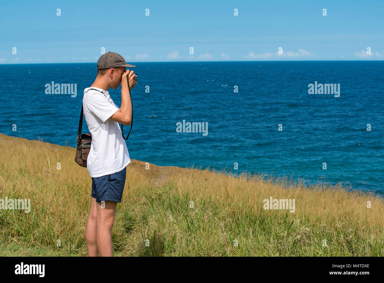 Un giovane uomo di scattare foto in prossimità dell'oceano con un analogo SLR Fotocamera Foto Stock