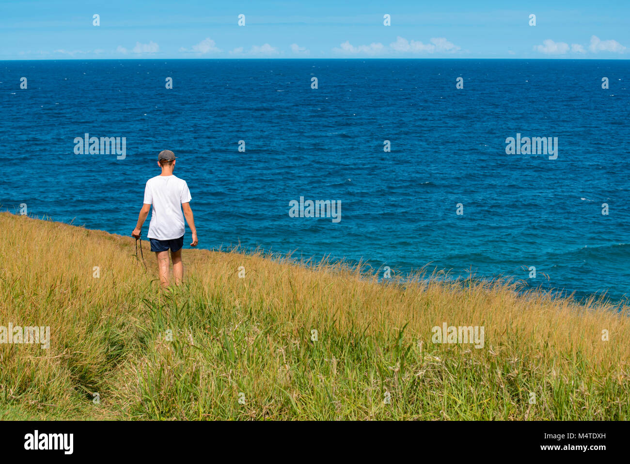Un giovane uomo che cammina lungo un sentiero stretto attraverso erba lunga in prossimità dell'oceano con un analogo SLR Fotocamera Foto Stock