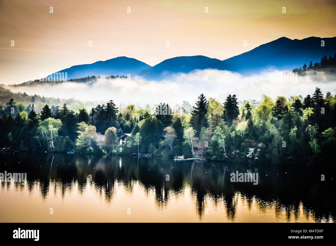 Riflessi di Montagne Adirondack e la mattina presto la nebbia e la nebbia sullo specchio del lago in Lake Placid, New York. Foto Stock