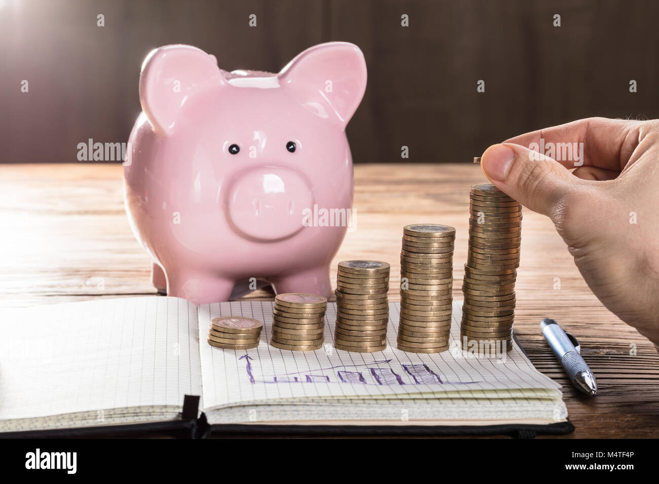 Close-up di una persona che immetta moneta sulla moneta impilato con grafico nella parte anteriore del Piggybank Foto Stock