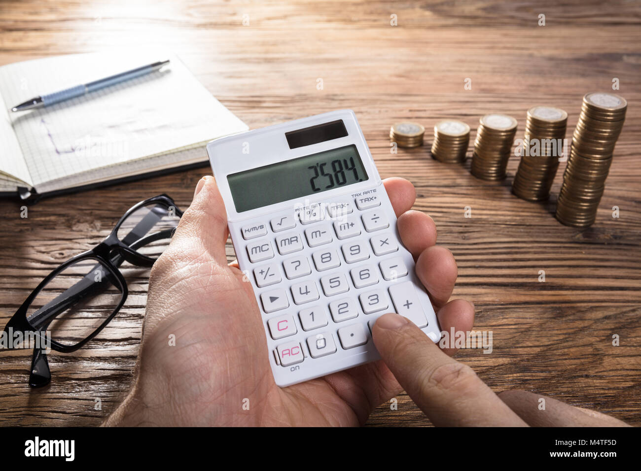 Close-up di una persona il calcolo di profitto sulla calcolatrice con Notebook, occhiali e Coin impilati Foto Stock