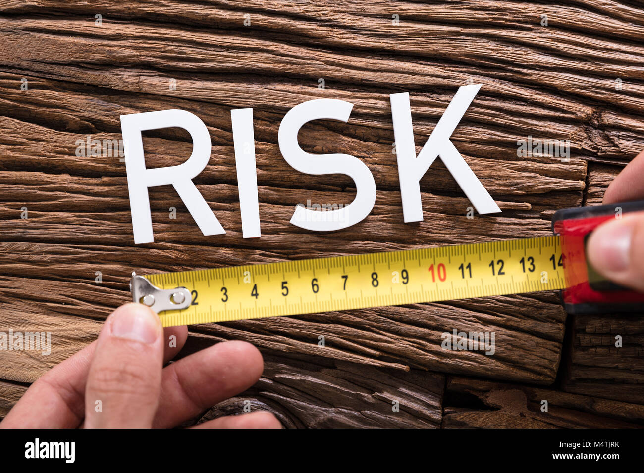 Close-up di una persona in possesso di nastro di misurazione vicino a rischio il testo vicino al tavolo di legno Foto Stock