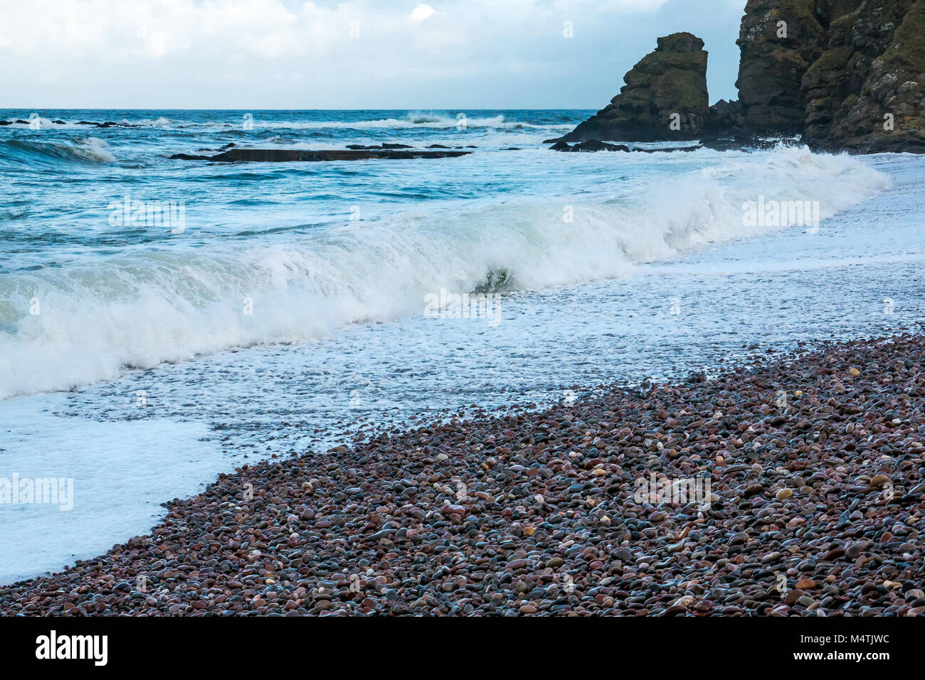 Nethermill, Aberdeenshire, Scotland, Regno Unito. Venti forti picchi di creare nel mare del Nord con grandi onde che si infrangono sulla riva di ghiaia Foto Stock