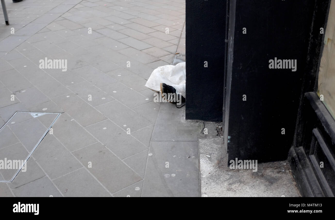 Brighton Regno Unito Febbraio 2018 - senzatetto uomo dorme in North Street shop portale con piedi spuntavano sul marciapiede Foto Stock
