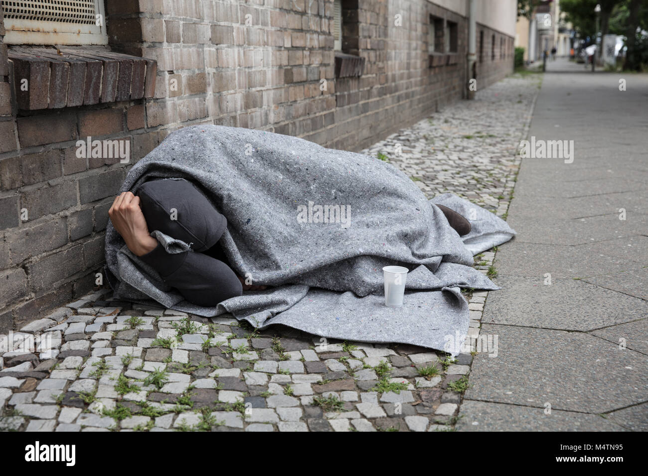 Uomo senza tetto coperto con una coperta di dormire sulla strada in città Foto Stock